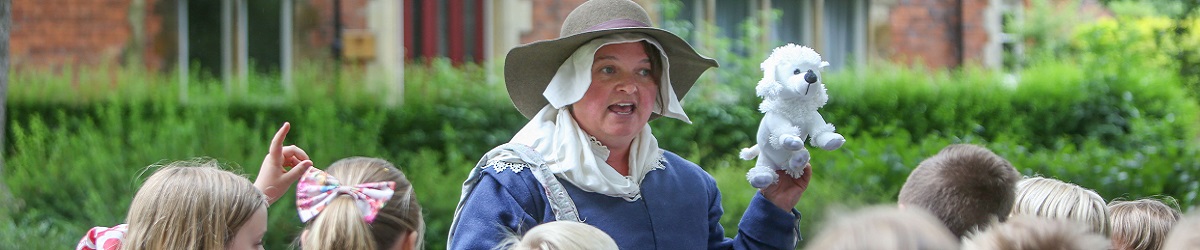 A member of the Learning Team dressed as a 17th century townsperson speaks to a group of children with a puppet dog during a schools tour of Newark